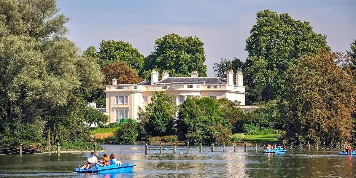 The Holme mansion in Regent’s Park, London, surrounded by trees and overlooking a lake with people boating in the foreground