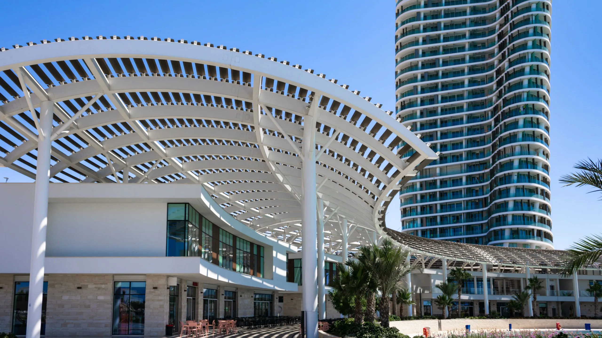 Modern beachfront architecture A modern beachfront building with a curved white canopy and a tall skyscraper in the background.