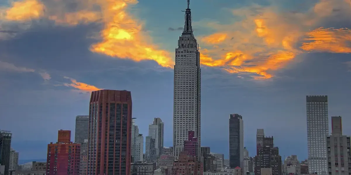 Empire State Building in New York City at sunset, with dramatic clouds and skyline in the background