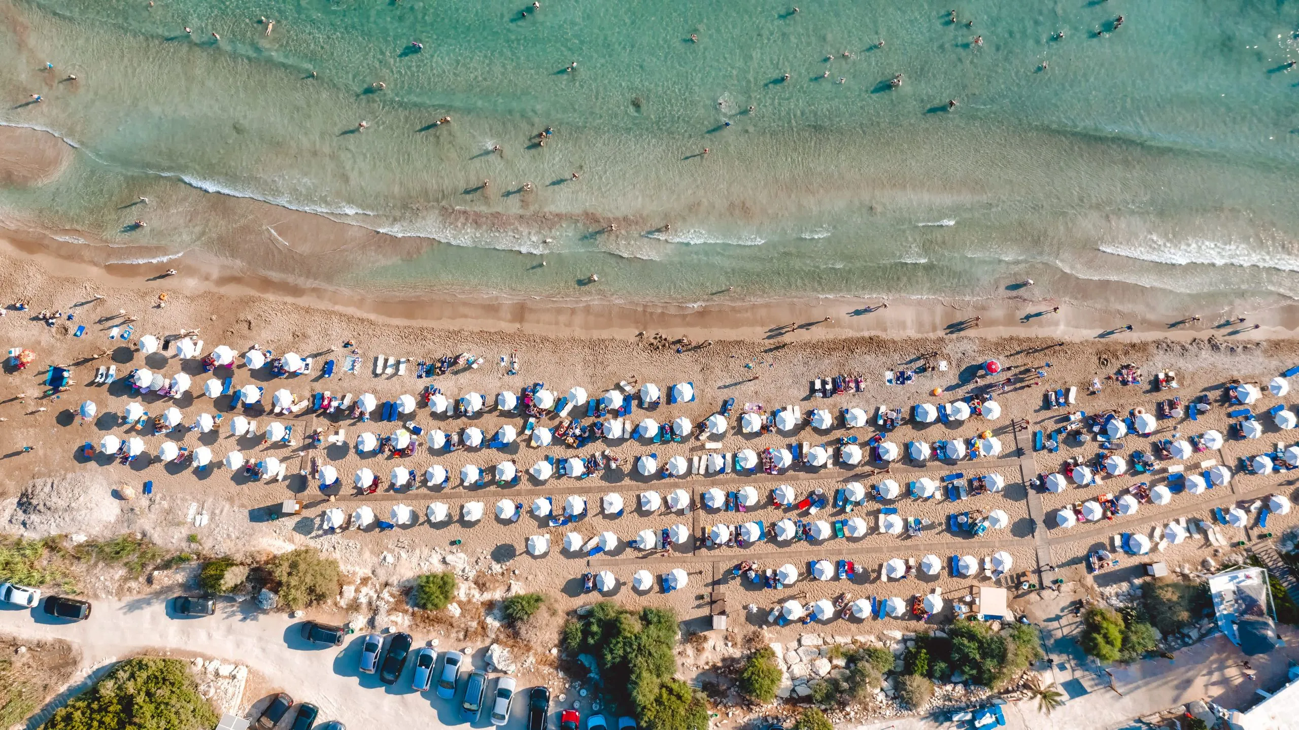 Summer Beach Scene in cyprus A sandy beach lined with white umbrellas and sunbathers, lapped by clear blue waves.