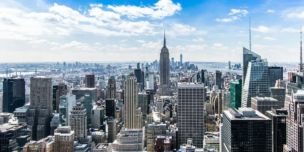 Panoramic view of Midtown Manhattan with Empire State Building centered, under blue sky and scattered clouds