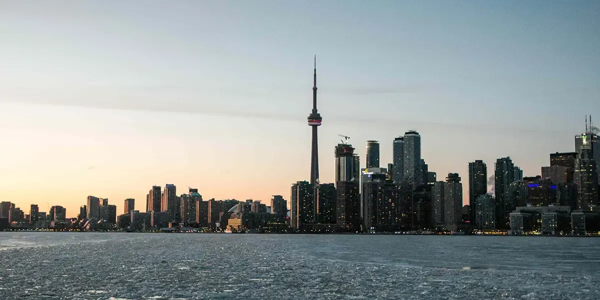 Toronto skyline at sunset with CN Tower in the center, viewed across a calm body of water
