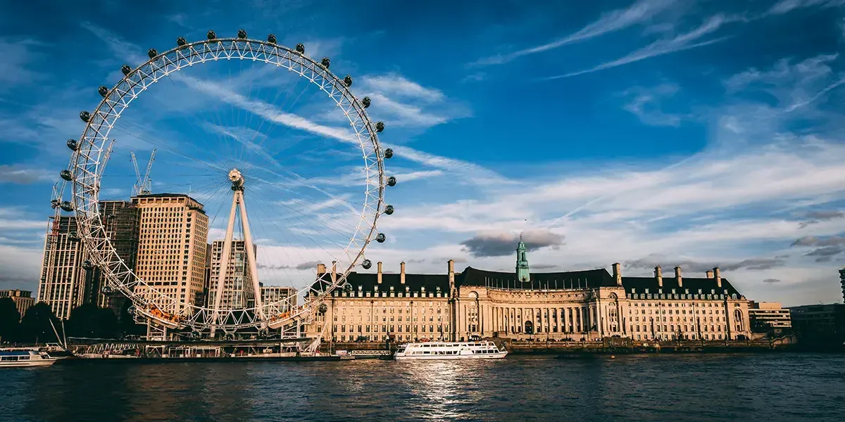 The London Eye observation wheel and County Hall on the River Thames at sunset with tour boats in foreground